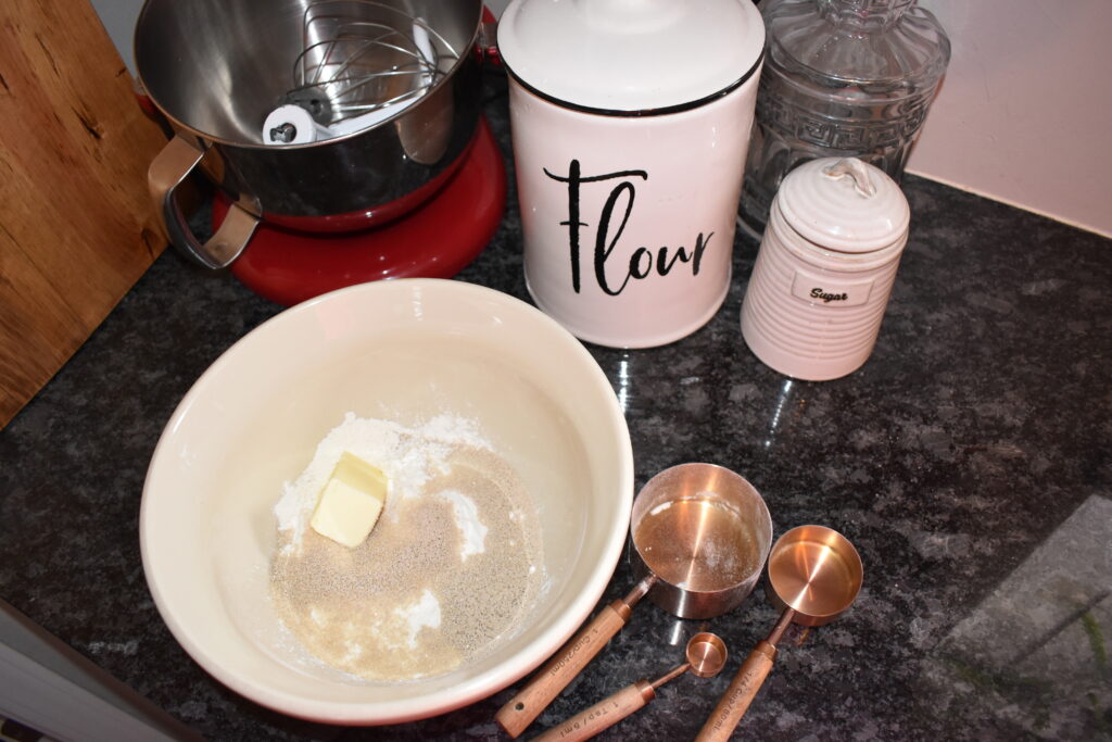 Flour and yeast in a mixing bowl with measuring cups beside it