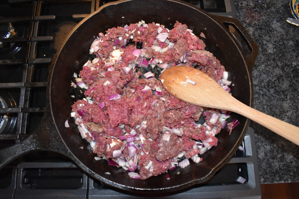 Ground deer cooking in a cast iron skillet with onions