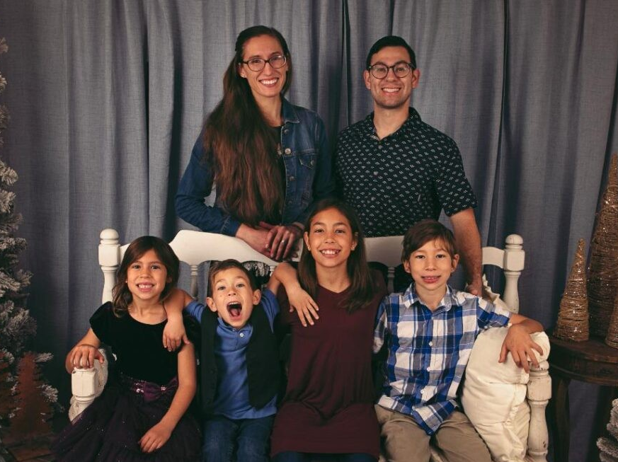 Family of six, parents standing behind the four children sitting on a bench