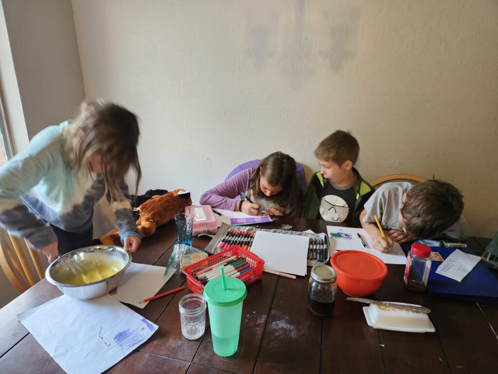 Children around the dining room table with craft supplies scattered all over the table