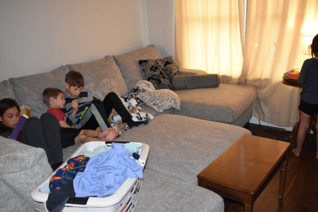 Children lounging on couch with basket of laundry to be folded