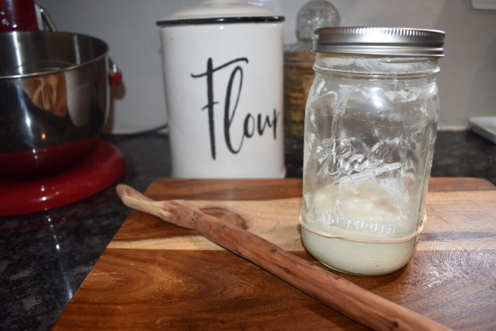 Sourdough starter in a jar with a flour jar behind it and mixing spoon next to it