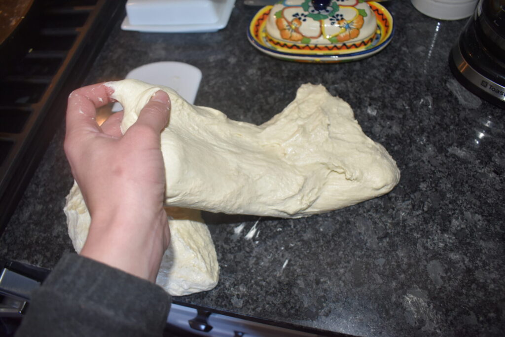 A woman stretching and folding a sourdough loaf in the other direction