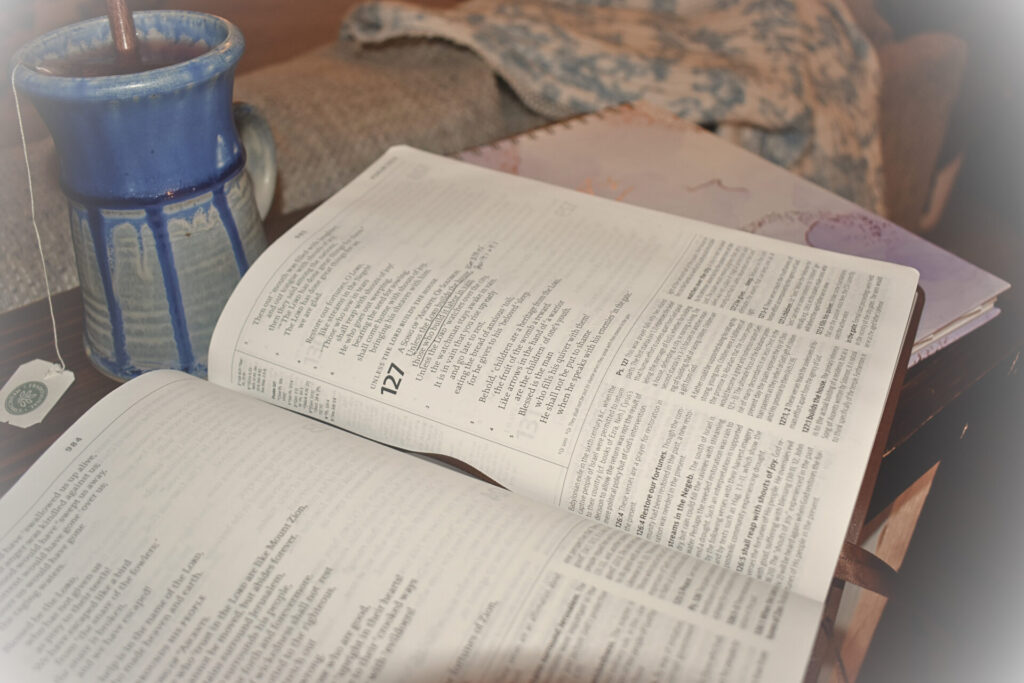 Bibe open to an underlined passage with a note pad and tea mug