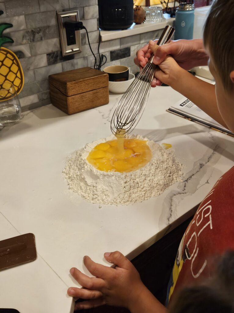 Young boy whisking eggs in a flour well to make pasta
