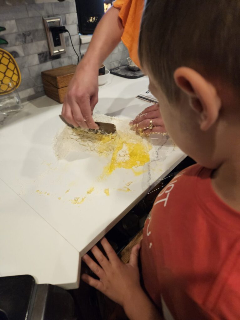 using a scraper to mix the eggs in the flour to make the pasta dough