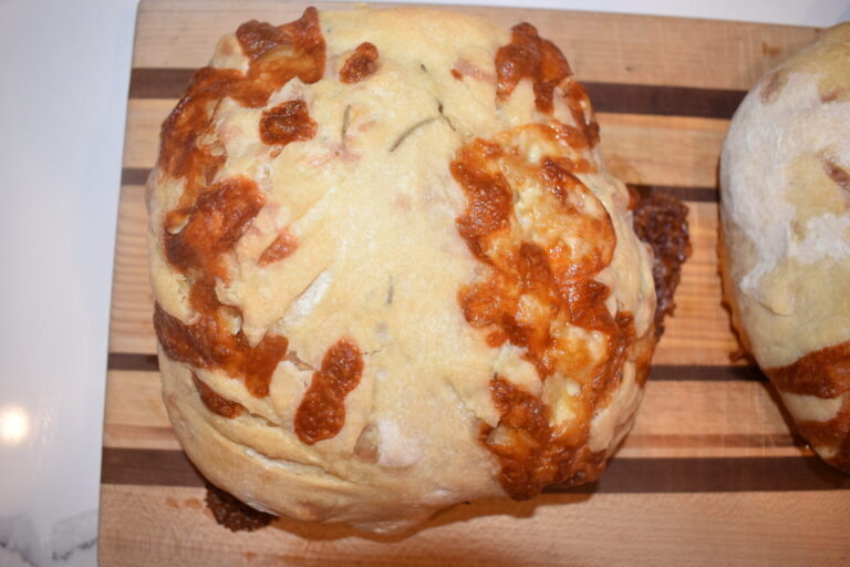 Rosemary cheese sourdough loaf sitting on a cutting board